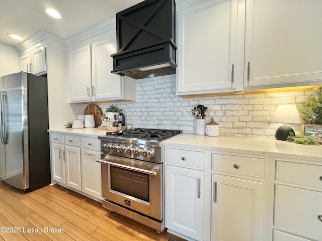 kitchen with backsplash, light wood-style flooring, stainless steel appliances, white cabinetry, and wall chimney exhaust hood