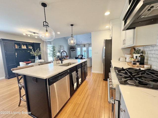 kitchen featuring light wood-type flooring, an island with sink, a sink, appliances with stainless steel finishes, and exhaust hood