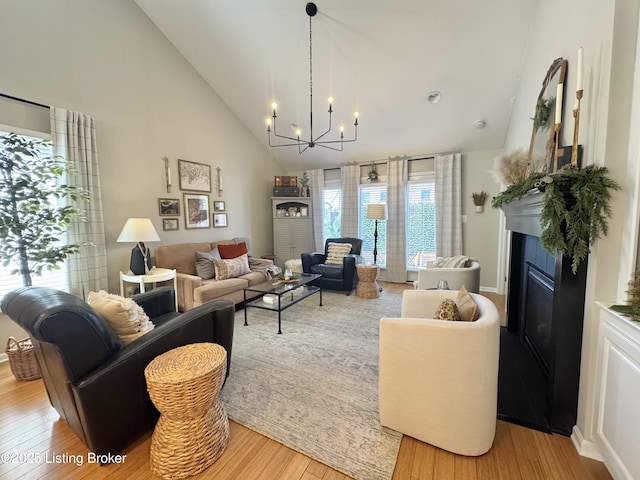 living area featuring a glass covered fireplace, an inviting chandelier, high vaulted ceiling, and light wood-style floors