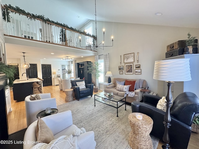 living area with light wood-type flooring, high vaulted ceiling, and an inviting chandelier