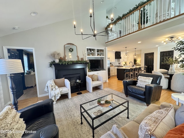 living area featuring a glass covered fireplace, a notable chandelier, light wood-type flooring, and high vaulted ceiling