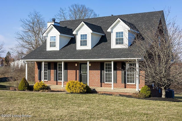 new england style home with a front yard, covered porch, brick siding, and a shingled roof