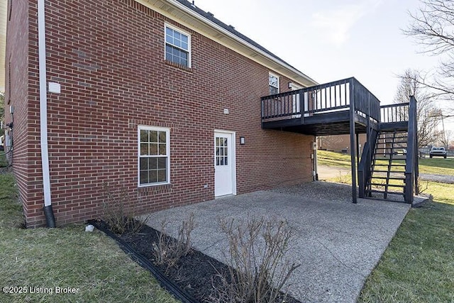 exterior space featuring a deck, a patio, a yard, brick siding, and stairs