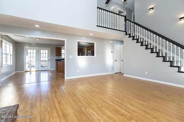 unfurnished living room featuring light wood-type flooring, baseboards, ceiling fan, and stairway