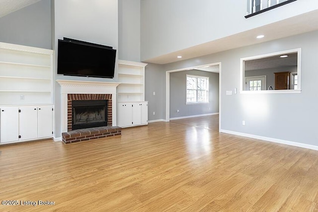 unfurnished living room featuring light wood-type flooring, baseboards, a high ceiling, and a brick fireplace