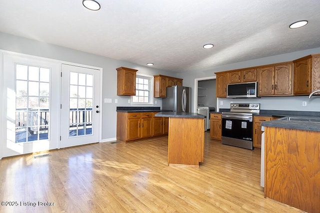 kitchen featuring a kitchen island, a sink, stainless steel appliances, dark countertops, and light wood-type flooring