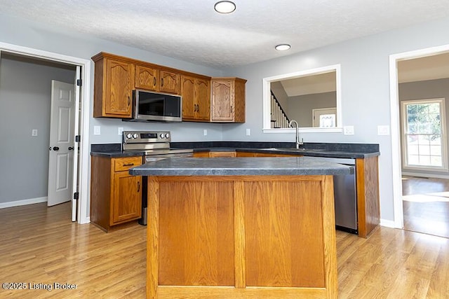 kitchen featuring a sink, a kitchen island, appliances with stainless steel finishes, brown cabinetry, and light wood finished floors