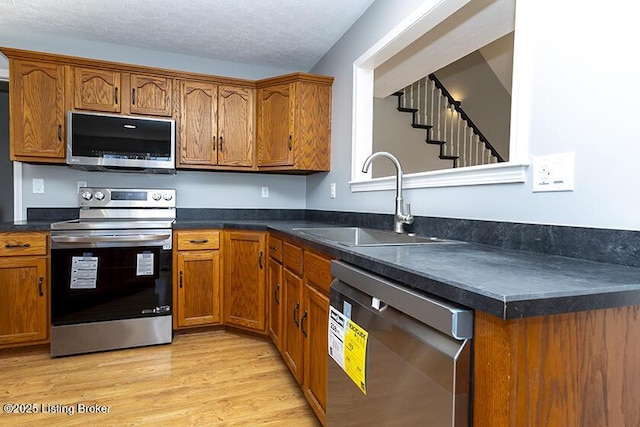 kitchen featuring a sink, stainless steel appliances, light wood-style floors, and brown cabinetry