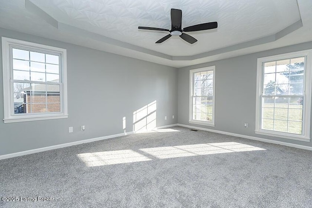 spare room featuring a ceiling fan, visible vents, baseboards, a tray ceiling, and carpet flooring