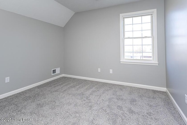 carpeted empty room with visible vents, baseboards, and lofted ceiling