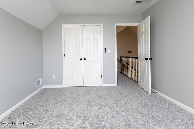 unfurnished bedroom with carpet, visible vents, baseboards, vaulted ceiling, and a closet