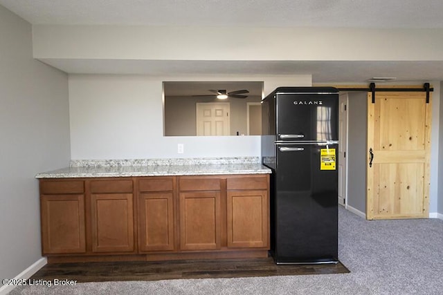 kitchen featuring baseboards, a barn door, brown cabinets, freestanding refrigerator, and a ceiling fan