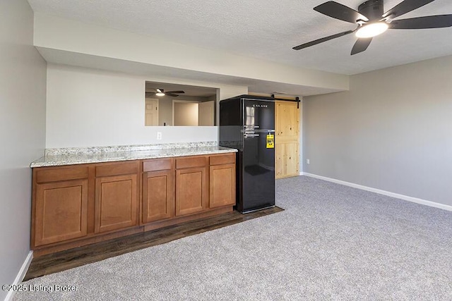 kitchen with brown cabinets, a textured ceiling, dark carpet, a barn door, and baseboards