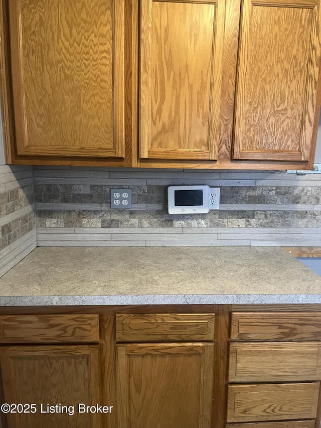 interior details featuring light countertops, brown cabinetry, and backsplash