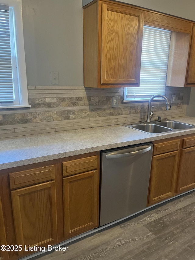 kitchen with brown cabinetry, a sink, decorative backsplash, light countertops, and stainless steel dishwasher