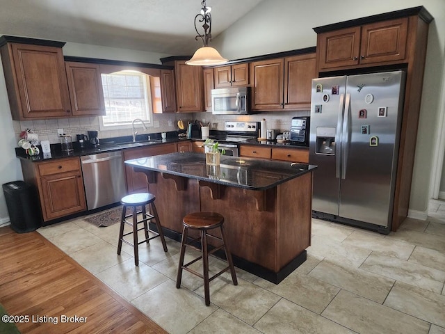 kitchen featuring tasteful backsplash, a kitchen island, vaulted ceiling, stainless steel appliances, and a sink