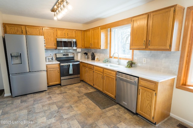 kitchen featuring tasteful backsplash, light countertops, appliances with stainless steel finishes, stone finish floor, and a sink