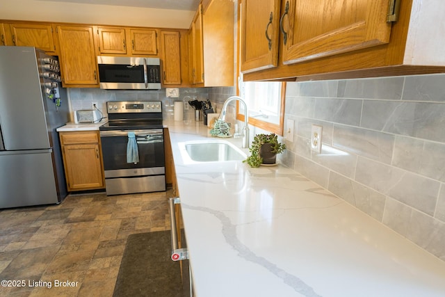 kitchen featuring a sink, stainless steel appliances, stone finish flooring, tasteful backsplash, and brown cabinets