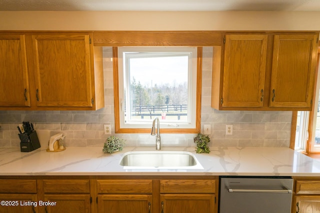 kitchen featuring dishwasher, decorative backsplash, light stone counters, and a sink