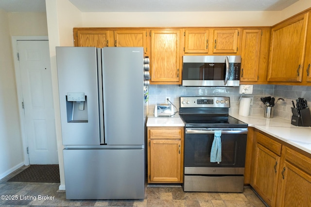 kitchen with backsplash, light countertops, brown cabinets, appliances with stainless steel finishes, and stone finish floor