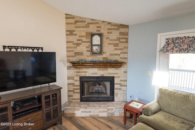 living room with a stone fireplace, lofted ceiling, and wood finished floors