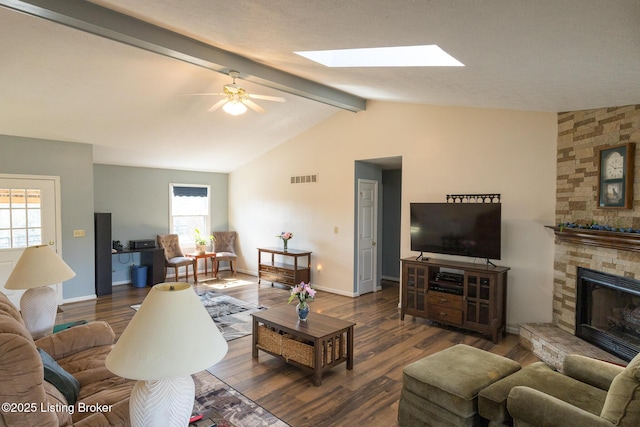 living room featuring visible vents, a stone fireplace, wood finished floors, and vaulted ceiling with beams