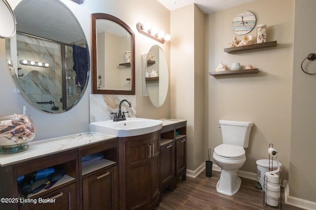 bathroom with baseboards, toilet, wood finished floors, vanity, and a shower