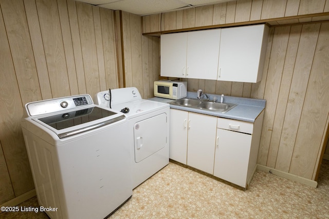 laundry room with cabinet space, wooden walls, separate washer and dryer, and a sink