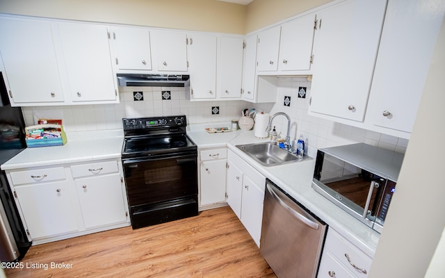 kitchen with light wood-type flooring, a sink, under cabinet range hood, tasteful backsplash, and appliances with stainless steel finishes