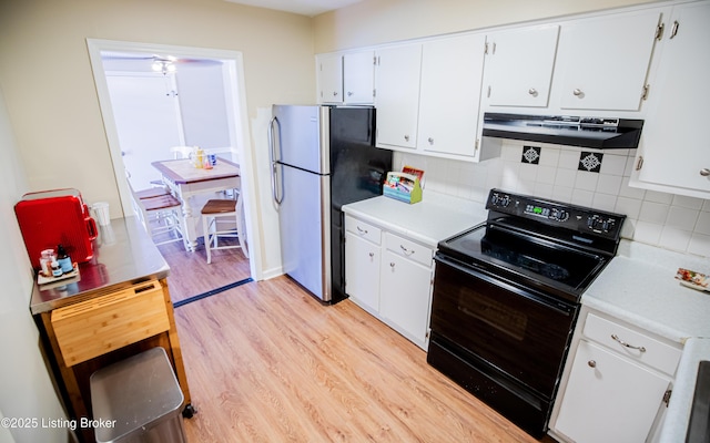 kitchen with black range with electric stovetop, under cabinet range hood, freestanding refrigerator, light wood-style floors, and light countertops