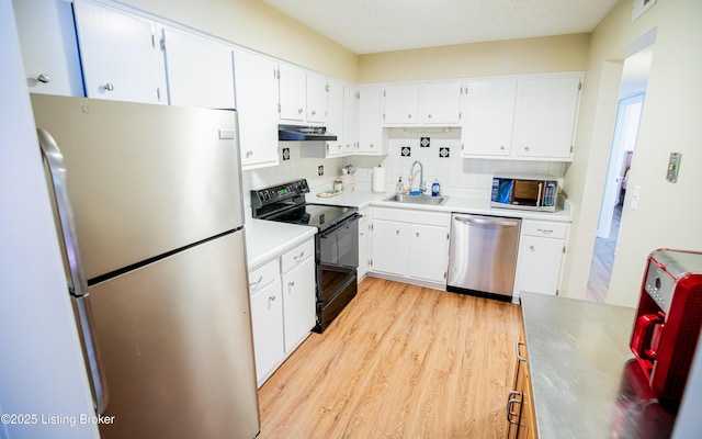 kitchen with tasteful backsplash, under cabinet range hood, appliances with stainless steel finishes, light wood-style floors, and a sink