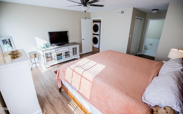 bedroom with visible vents, stacked washer and clothes dryer, wood finished floors, connected bathroom, and ceiling fan