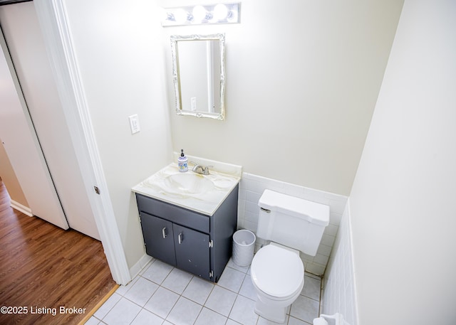 half bathroom with tile patterned flooring, toilet, vanity, and tile walls