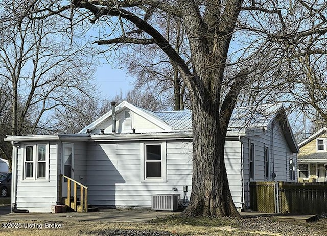 rear view of property featuring cooling unit, fence, metal roof, and entry steps