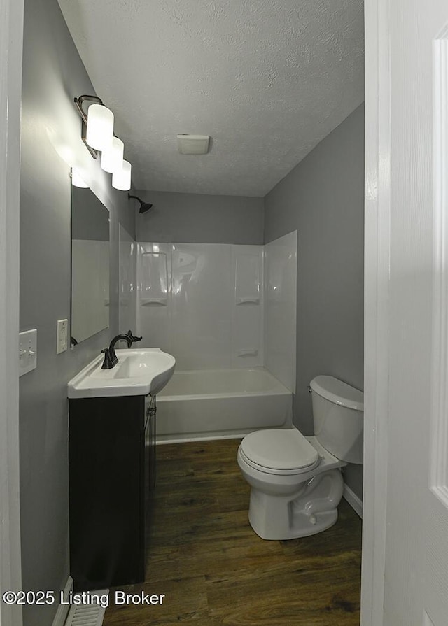 bathroom featuring toilet, a textured ceiling, wood finished floors, washtub / shower combination, and vanity