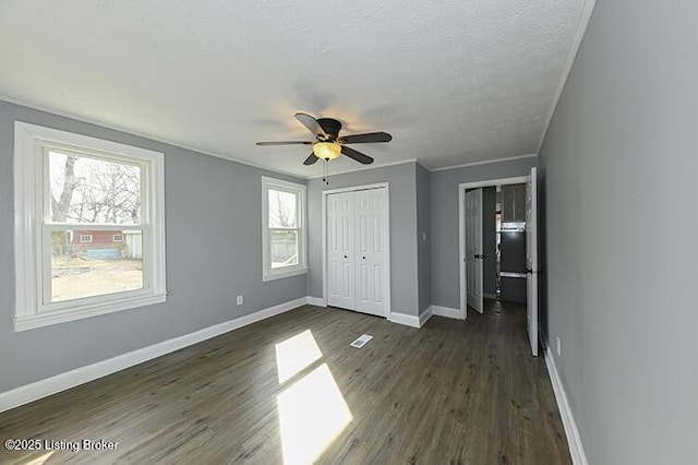 unfurnished bedroom featuring dark wood-type flooring, ornamental molding, a textured ceiling, baseboards, and ceiling fan