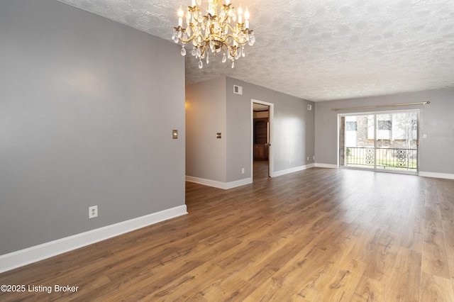 unfurnished living room with visible vents, a textured ceiling, wood finished floors, an inviting chandelier, and baseboards