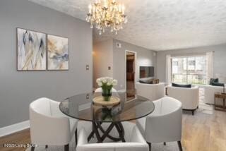 dining space featuring a chandelier, a textured ceiling, baseboards, and wood finished floors