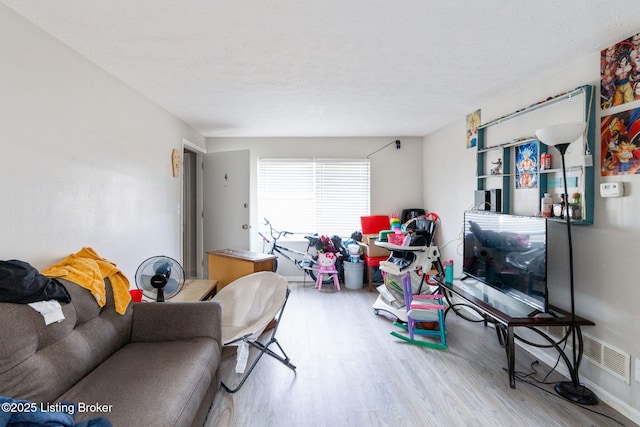 living area with visible vents, wood finished floors, baseboards, and a textured ceiling