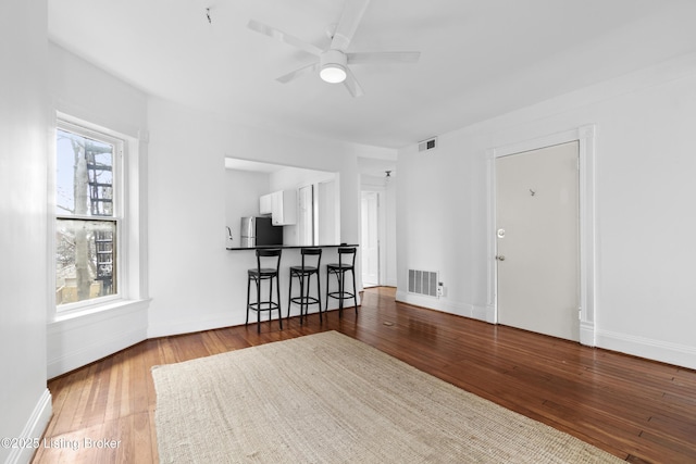 unfurnished living room featuring visible vents, baseboards, a ceiling fan, and wood-type flooring