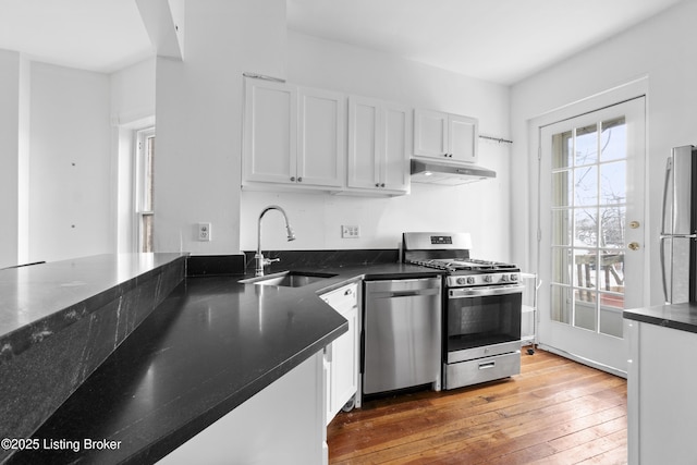 kitchen featuring under cabinet range hood, appliances with stainless steel finishes, light wood-style floors, white cabinets, and a sink