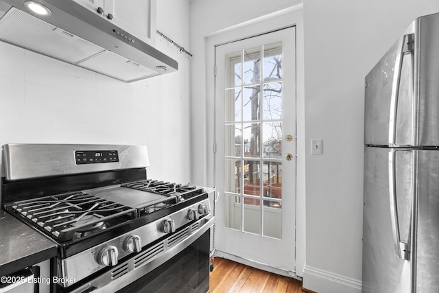 kitchen featuring under cabinet range hood, light wood-style flooring, baseboards, and appliances with stainless steel finishes