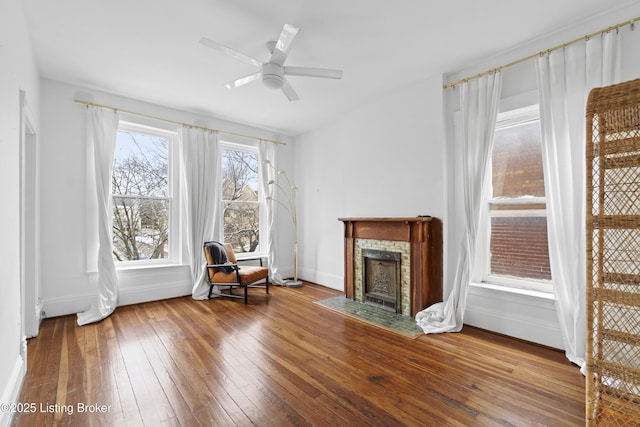 unfurnished room featuring baseboards, wood-type flooring, a ceiling fan, and a fireplace