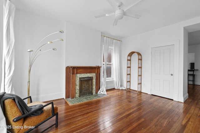 living area with baseboards, a tile fireplace, a ceiling fan, and hardwood / wood-style flooring