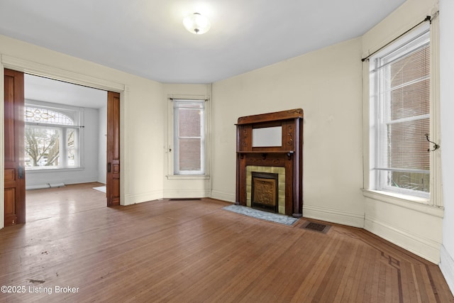 unfurnished living room with a tiled fireplace, visible vents, and wood finished floors