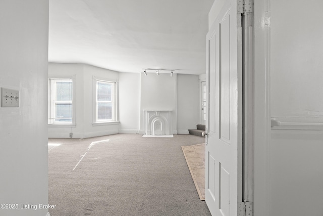 unfurnished living room featuring rail lighting, baseboards, and carpet flooring