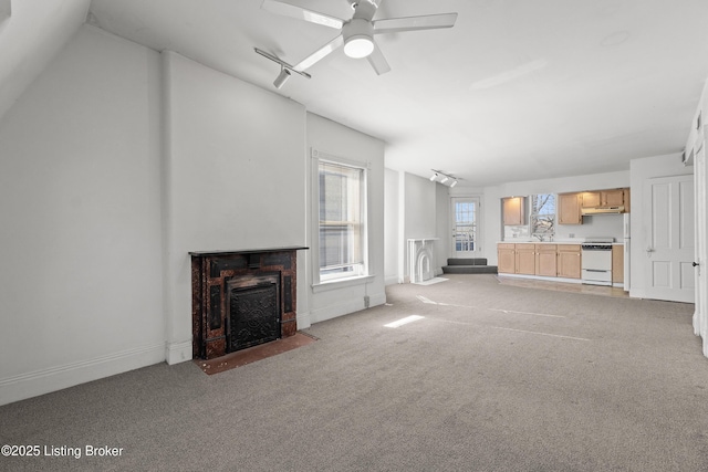 unfurnished living room featuring light carpet, a fireplace with flush hearth, rail lighting, and a ceiling fan