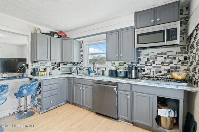 kitchen featuring backsplash, gray cabinets, appliances with stainless steel finishes, light wood-style flooring, and a sink