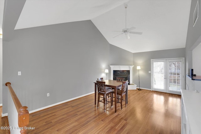 dining room with high vaulted ceiling, wood finished floors, a fireplace, baseboards, and ceiling fan