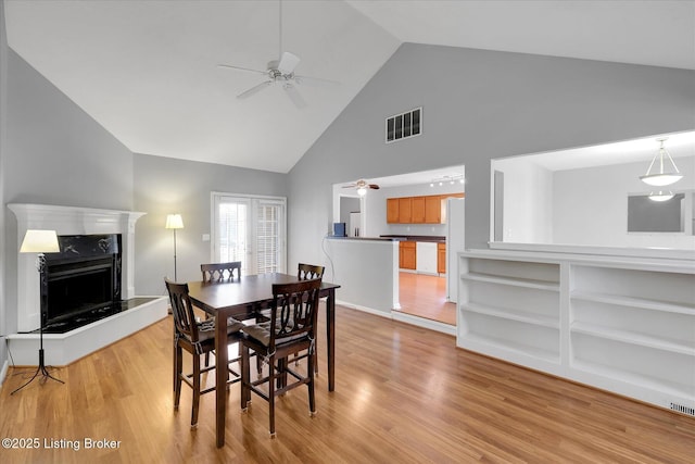 dining room with a high end fireplace, visible vents, ceiling fan, light wood-style flooring, and high vaulted ceiling